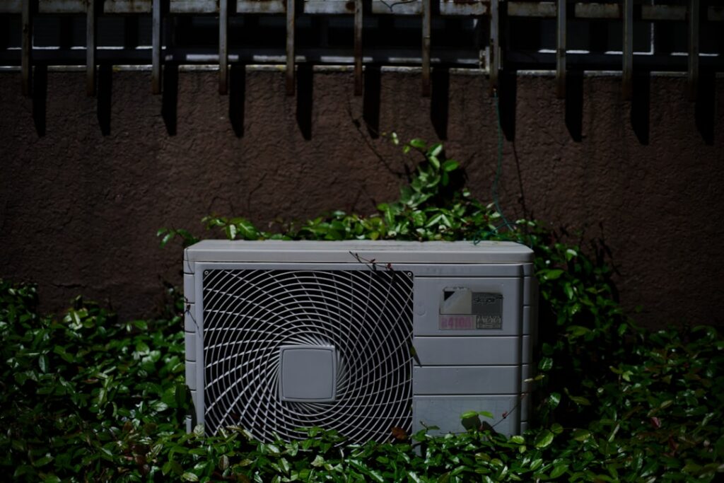 outdoor AC condenser unit with debris buildup and visible coil fins in a residential backyard